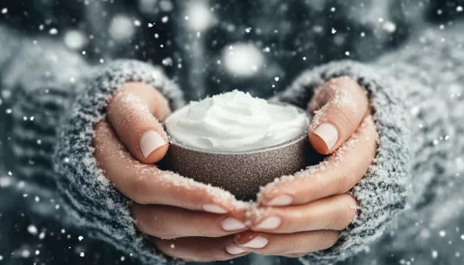 How to maintain glowing skin in winter: hands applying cream amidst a serene snowy winter backdrop