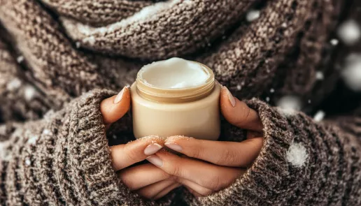 How to care for hands and lips in winter: person applying lip balm in a cozy winter setting to protect skin from dryness.